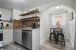 Kitchen featuring stainless steel dishwasher, light wood-style flooring, arched walkways, gray cabinets, and light stone countertops