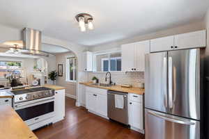 Kitchen featuring stainless steel appliances, butcher block countertops, island exhaust hood, and arched walkways