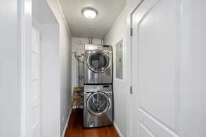 Laundry area featuring estacked washer and dryer, dark wood-style flooring, and electric panel