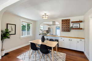 Dining space featuring arched walkways, dark wood-style flooring, and a textured ceiling