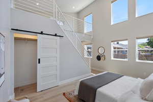 Bedroom featuring a barn door, light wood-type flooring, a towering ceiling, and recessed lighting