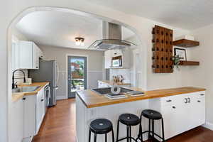Kitchen with butcher block countertops, island exhaust hood, dark wood-style flooring, white microwave, and decorative backsplash