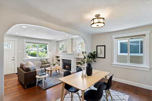 Dining area with arched walkways, dark wood-style floors, a glass covered fireplace, a textured ceiling, and recessed lighting