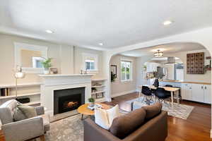 Living area with arched walkways, a fireplace with flush hearth, wood finished floors, recessed lighting, and a textured ceiling