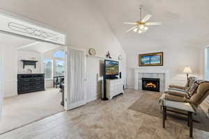 Living area featuring high vaulted ceiling, a high end fireplace, a ceiling fan, light carpet, and a decorative wall