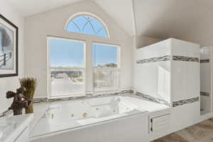 Bathroom featuring a jetted tub, vaulted ceiling, tiled shower, and vanity