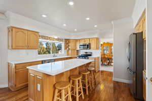Kitchen with appliances with stainless steel finishes, dark wood-style floors, a kitchen breakfast bar, crown molding, and a center island