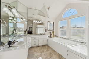 Bathroom with vaulted ceiling, a tub with jets, vanity, and a ceiling fan