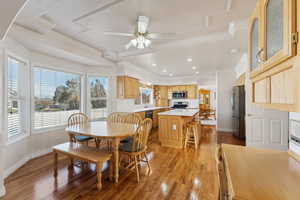 Dining space featuring light wood-type flooring, ornamental molding, ceiling fan, recessed lighting, and a raised ceiling