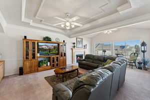 Living room with light colored carpet, ceiling fan, ornamental molding, a warm lit fireplace, and a textured ceiling