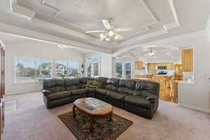 Living area featuring a ceiling fan, arched walkways, light colored carpet, crown molding, and a tray ceiling