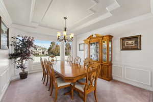 Dining space with a decorative wall, light carpet, a chandelier, crown molding, and a tray ceiling