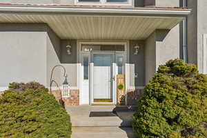 Entrance to property featuring stucco siding, stone siding, and a porch