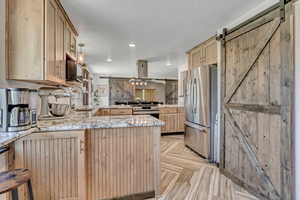 Kitchen featuring a barn door, appliances with stainless steel finishes, a peninsula, light brown cabinets, and island exhaust hood