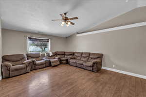 Living room with lofted ceiling, ceiling fan, wood finished floors, and a textured ceiling