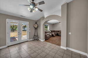 Tiled empty room with arched walkways, a ceiling fan, french doors, and lofted ceiling