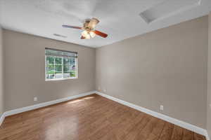 Empty room with attic access, wood finished floors, a ceiling fan, and a textured ceiling