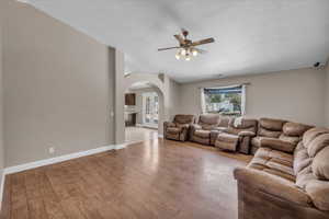 Living room featuring arched walkways, a ceiling fan, light wood finished floors, and a textured ceiling