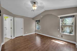Unfurnished bedroom with wood finished floors, multiple windows, lofted ceiling, and ceiling fan