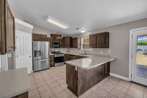 Kitchen with stainless steel appliances, a peninsula, vaulted ceiling, dark brown cabinetry, and light countertops