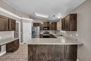 Kitchen featuring stainless steel appliances, vaulted ceiling, dark brown cabinets, light countertops, and light tile patterned flooring