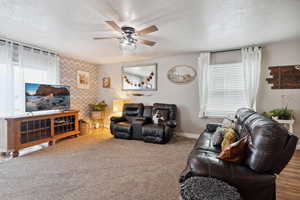 Carpeted living room with healthy amount of natural light, a textured ceiling, a ceiling fan, and an accent wall