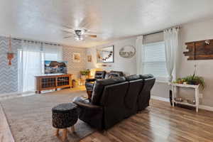 Living area with a textured ceiling, wallpapered walls, a ceiling fan, healthy amount of natural light, and wood finished floors
