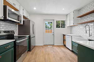 Kitchen with green cabinetry, stainless steel appliances, light countertops, open shelves, and recessed lighting