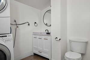 Half bath featuring estacked washer and dryer, vanity, and wood finished floors