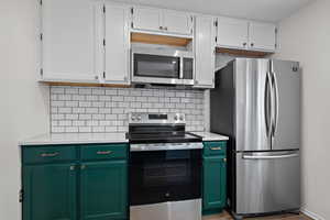 Kitchen with stainless steel appliances, light countertops, green cabinets, and decorative backsplash