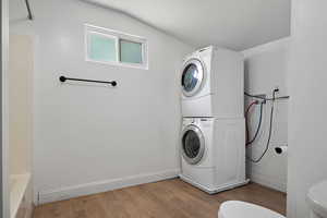 Washroom with stacked washing machine and dryer and wood finished floors