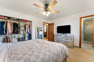 Carpeted bedroom with a closet, ceiling fan, ensuite bathroom, and baseboards