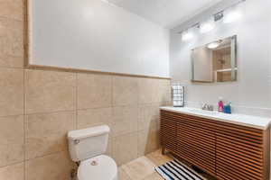 Bathroom with toilet, vanity, tile walls, tile patterned flooring, and wainscoting