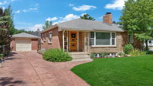 View of front of property with a chimney, a front yard, driveway, brick siding, and an outbuilding