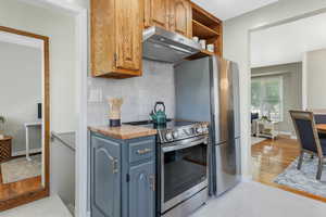 Kitchen with stainless steel electric range oven, under cabinet range hood, tasteful backsplash, blue cabinetry, and light wood-type flooring