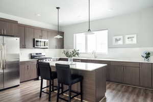 Kitchen with appliances with stainless steel finishes, a sink, a breakfast bar, dark wood-style floors, and recessed lighting