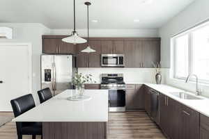 Kitchen featuring stainless steel appliances, a sink, an AC wall unit, wood finished floors, and a kitchen breakfast bar