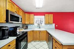 Kitchen with appliances with stainless steel finishes, a peninsula, light countertops, and brown cabinets