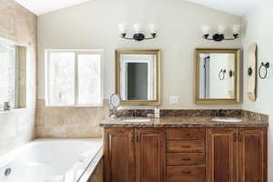 Full bath with plenty of natural light, double vanity, a bath, and lofted ceiling