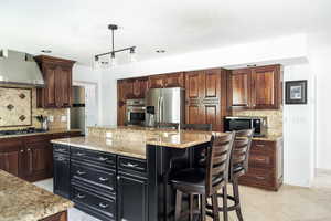 Kitchen featuring stainless steel appliances, wall chimney range hood, backsplash, and a center island