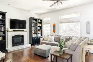 Living room with a ceiling fan, dark wood-style floors, and a brick fireplace