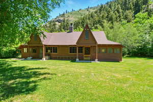 View of front of property featuring a front yard, faux log siding, a chimney, and roof with shingles