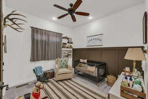 Bedroom featuring a decorative wall, a crib, recessed lighting, light colored carpet, and ceiling fan