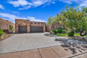 Pueblo-style home with a garage, driveway, stucco siding, and stone siding