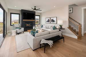 Living room featuring light wood-style floors, ceiling fan, recessed lighting, stairs, and a large fireplace