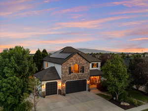View of front of house featuring stone siding, driveway, roof mounted solar panels, and stucco siding