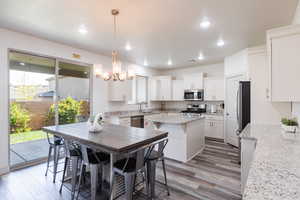 Kitchen with appliances with stainless steel finishes, a chandelier, a kitchen island, white cabinets, and light wood-style floors