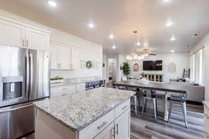 Kitchen with stainless steel refrigerator with ice dispenser, open floor plan, a kitchen island, dark wood-style flooring, and white cabinets