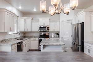 Kitchen with stainless steel appliances, a chandelier, white cabinets, a kitchen island, and recessed lighting