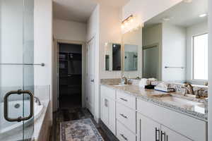 Bathroom featuring double vanity, a shower stall, wood finished floors, a garden tub, and a walk in closet